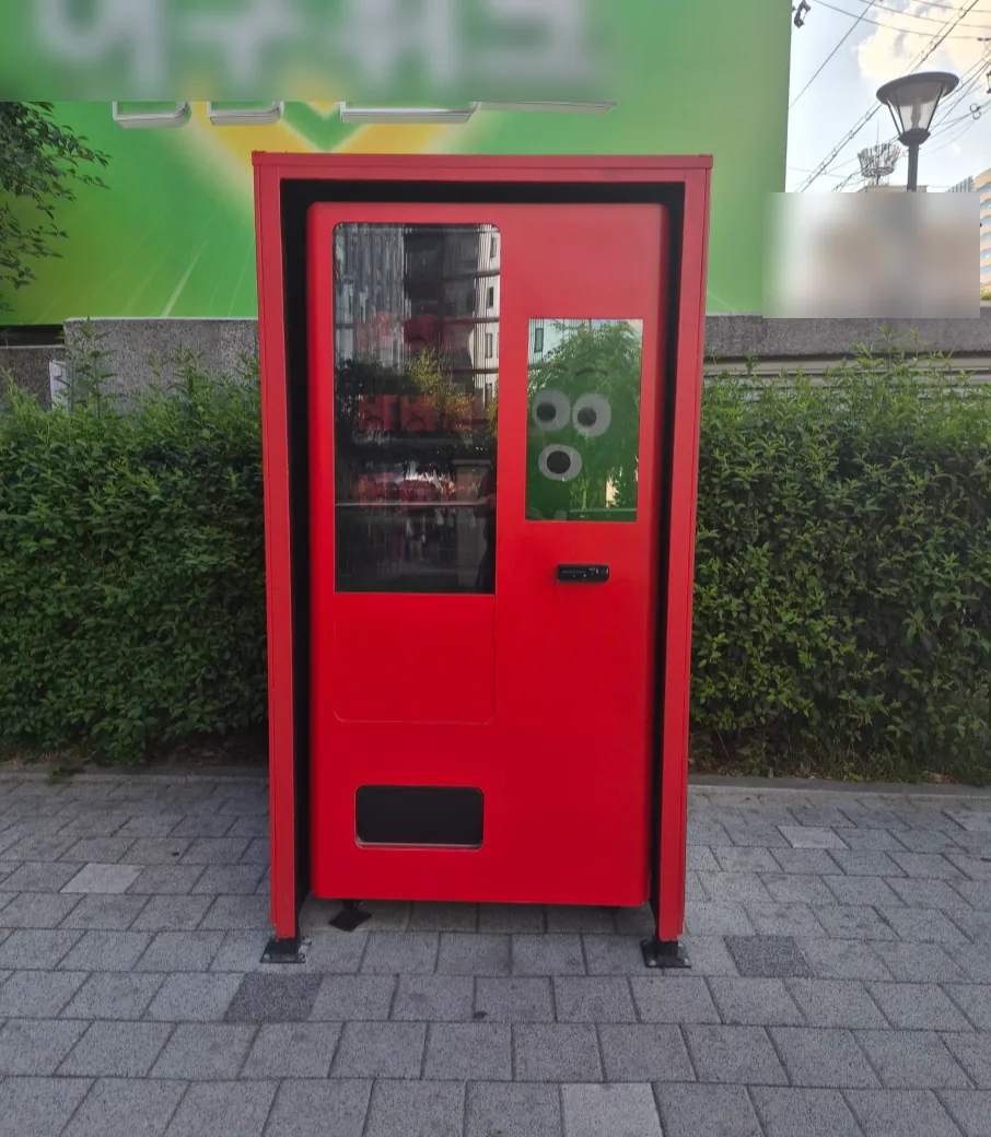 보도블록 위 화단 앞에 설치한 빨간색 외장의 자판기